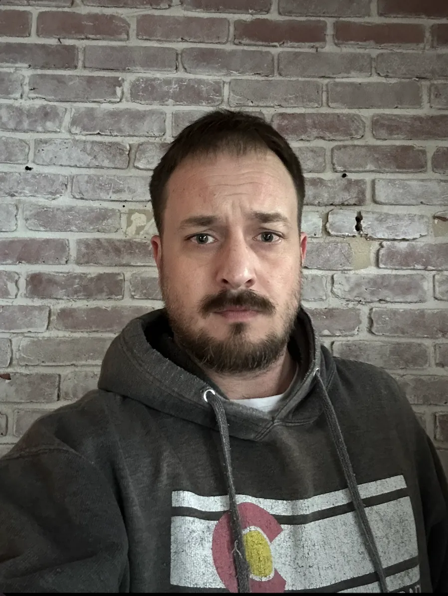 Alex Lamy in a gray hoodie in front of a brick wall